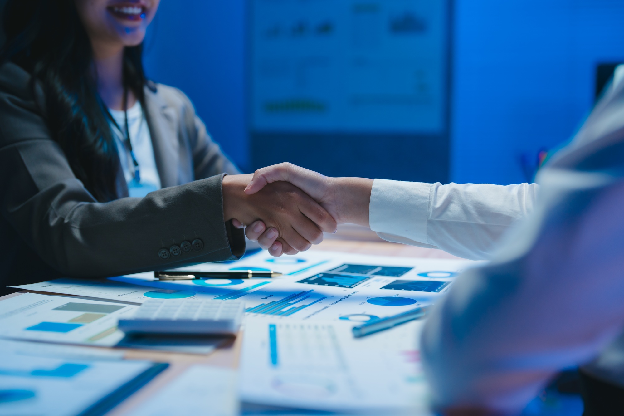 Businesswomen shaking hands after successful meeting over financial charts